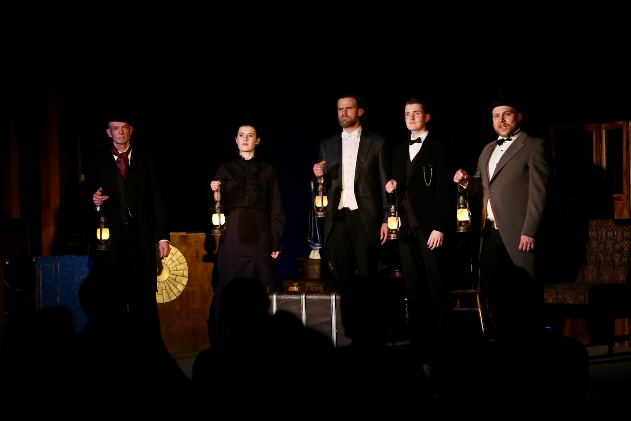 A line of actors hold lanterns