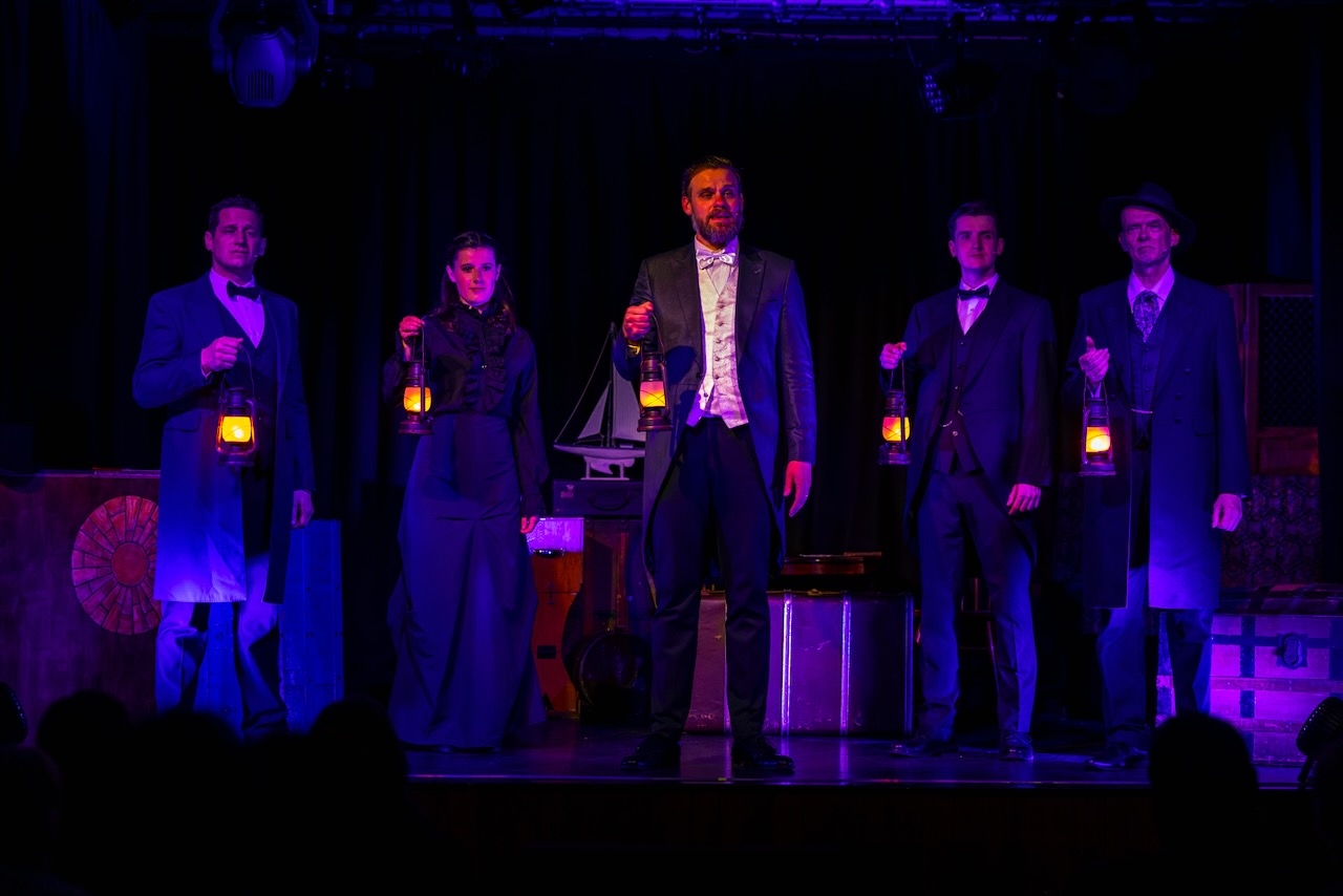 A line of actors hold lanterns in a dim atmospheric night scene