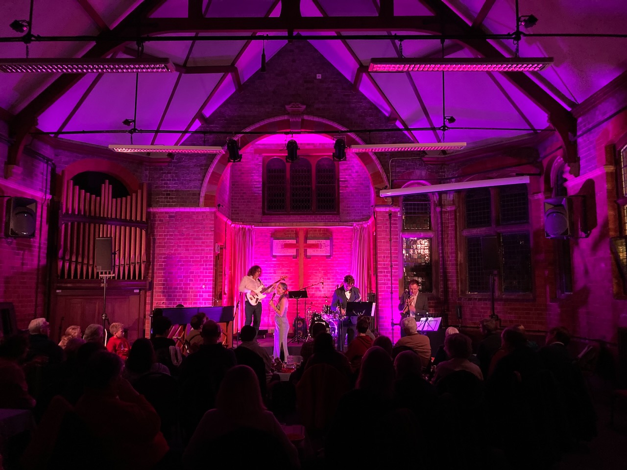 Wide church interior with The Roots of Jazz performing under pink lighting