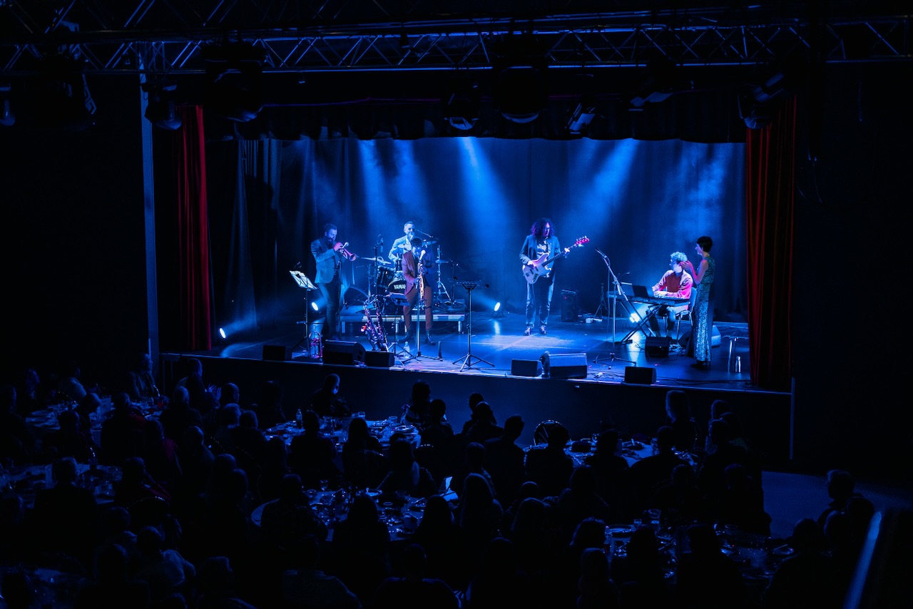 The Roots of Jazz band performing on a theatre stage with blue lighting