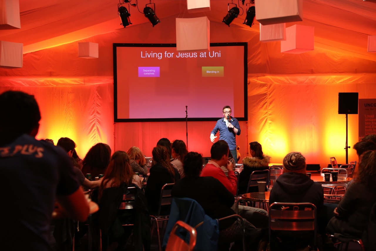 A presenter stands in front of an orange backdrop