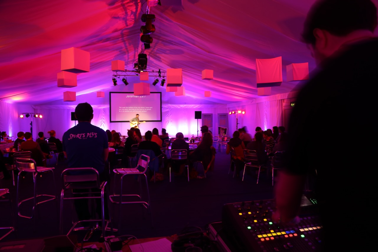 A sound engineer at work with a man with a guitar on stage and purple lighting